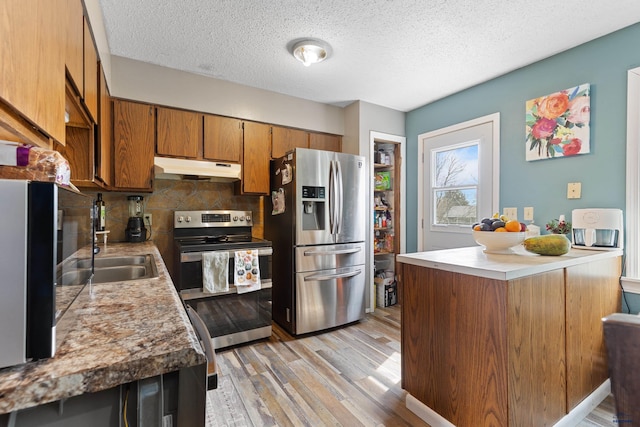 kitchen featuring light wood-style flooring, decorative backsplash, under cabinet range hood, appliances with stainless steel finishes, and brown cabinets