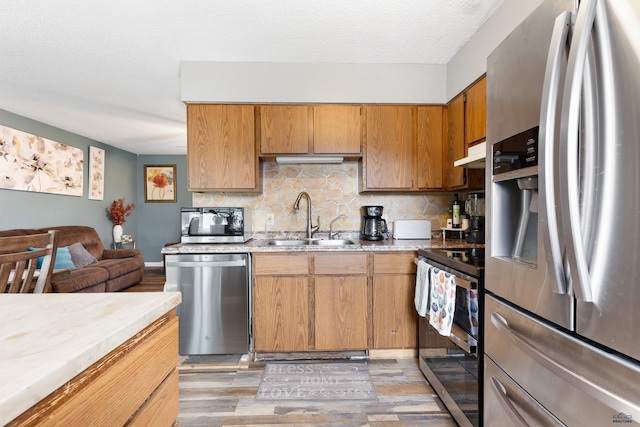 kitchen with a sink, under cabinet range hood, backsplash, stainless steel appliances, and light countertops