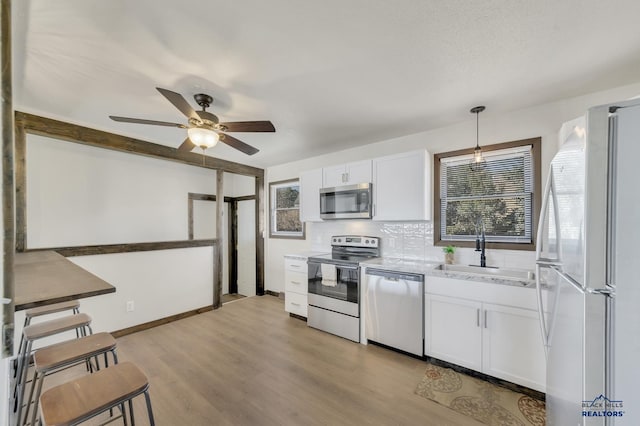 kitchen with light wood-style flooring, a sink, appliances with stainless steel finishes, white cabinetry, and backsplash