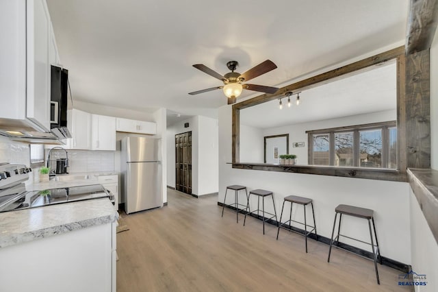 kitchen featuring freestanding refrigerator, decorative backsplash, white cabinets, a kitchen bar, and light wood-type flooring