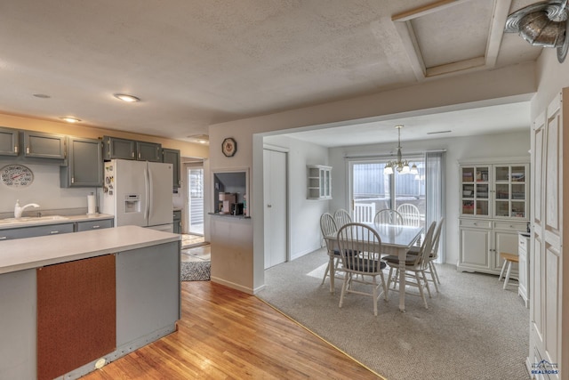 kitchen featuring light wood finished floors, pendant lighting, light countertops, white fridge with ice dispenser, and a sink