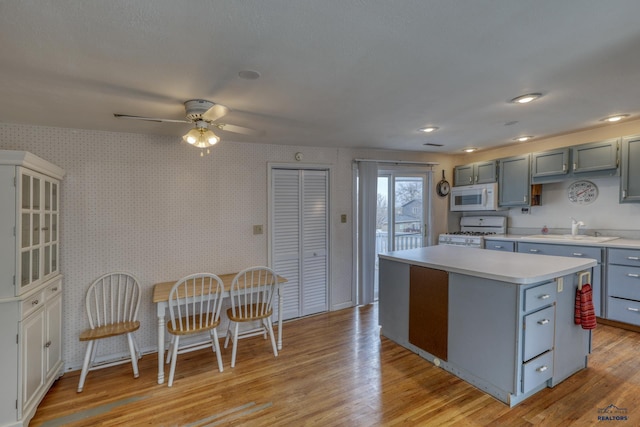 kitchen featuring wallpapered walls, white appliances, light wood finished floors, and a sink