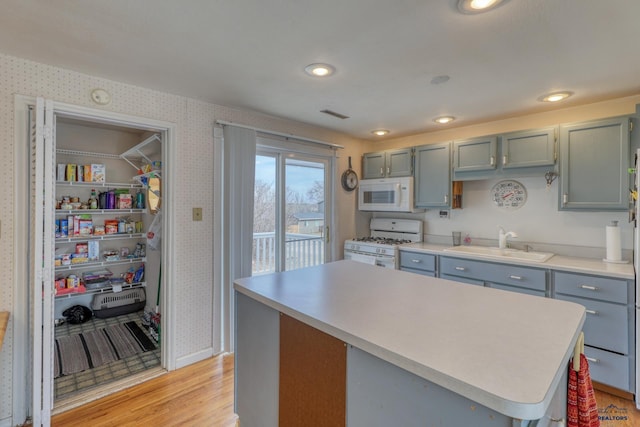 kitchen with white appliances, wallpapered walls, a sink, light countertops, and light wood-style floors