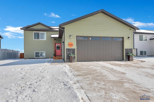 view of front of home with stone siding, a garage, and fence