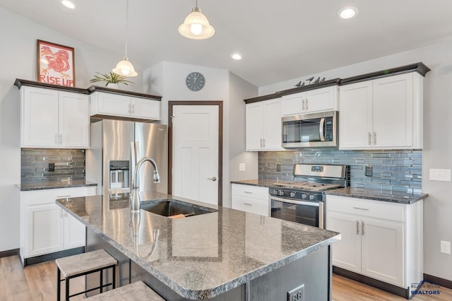 kitchen featuring light wood finished floors, dark stone countertops, appliances with stainless steel finishes, and a sink