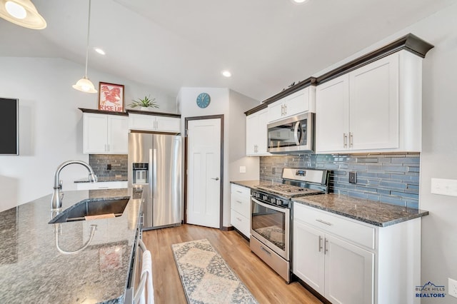 kitchen featuring lofted ceiling, dark stone countertops, light wood-style flooring, stainless steel appliances, and a sink