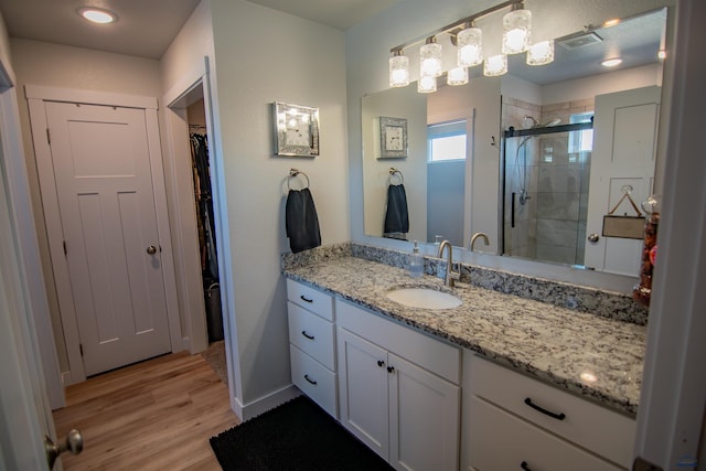 bathroom with visible vents, a walk in closet, wood finished floors, a shower stall, and vanity