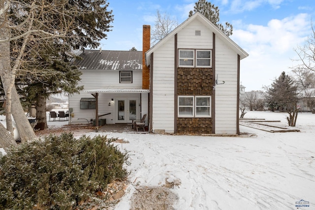 snow covered property with french doors, a chimney, and metal roof