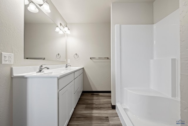 full bath with wood finished floors, double vanity, a sink, a shower, and a textured wall