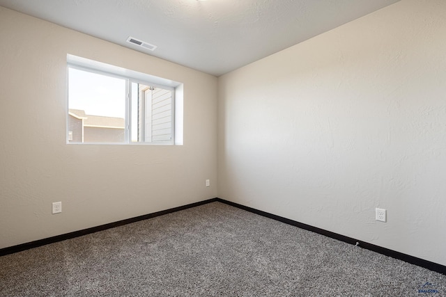 carpeted spare room with baseboards, visible vents, and a textured wall