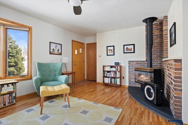 sitting room with ceiling fan, a wood stove, baseboards, and wood finished floors