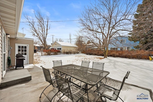 snow covered patio with outdoor dining area, fence, and grilling area