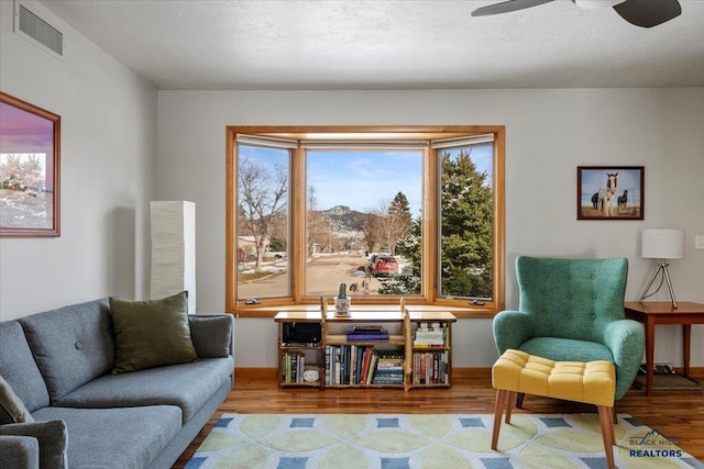 living area featuring visible vents, a ceiling fan, a textured ceiling, wood finished floors, and baseboards