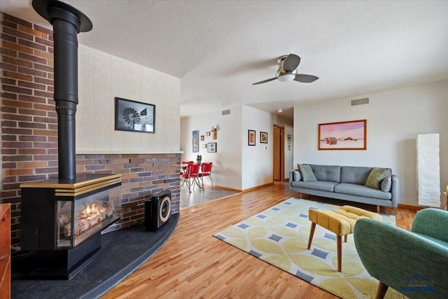 living room featuring a wood stove, wood finished floors, visible vents, and ceiling fan