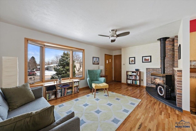 living area featuring a textured ceiling, a wood stove, ceiling fan, and wood finished floors