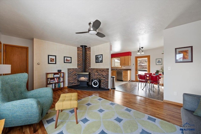 living room featuring a ceiling fan, wood finished floors, baseboards, a wood stove, and a textured ceiling