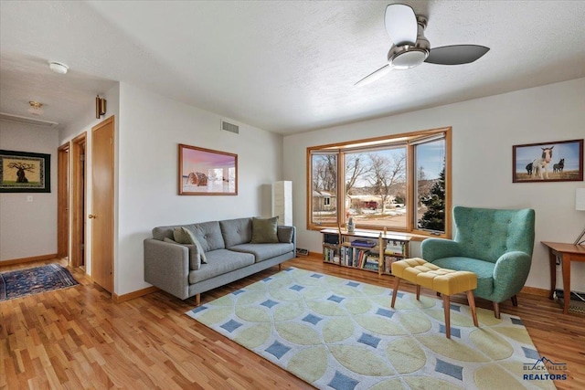 living area with visible vents, baseboards, ceiling fan, light wood-style floors, and a textured ceiling