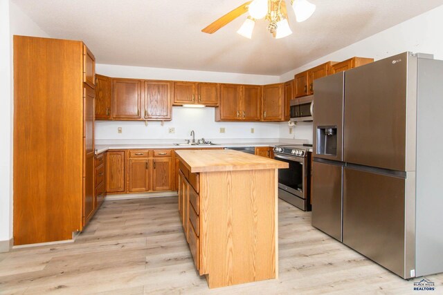 kitchen featuring a sink, butcher block countertops, stainless steel appliances, light wood-type flooring, and a center island