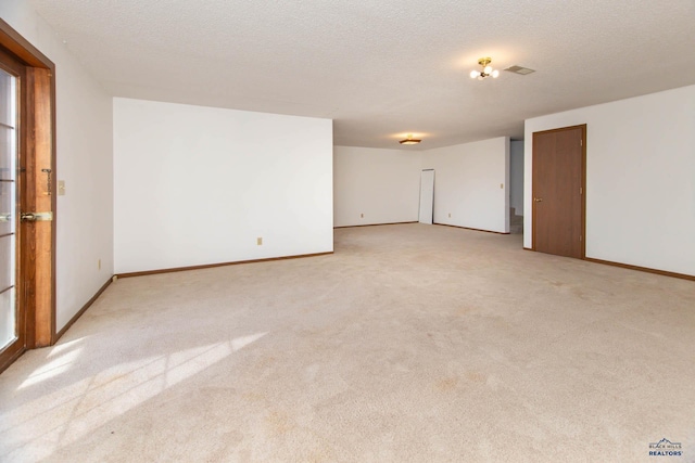 empty room with light carpet, visible vents, a textured ceiling, and baseboards