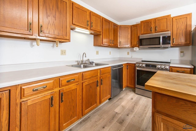 kitchen featuring a sink, light wood-style flooring, brown cabinetry, and stainless steel appliances