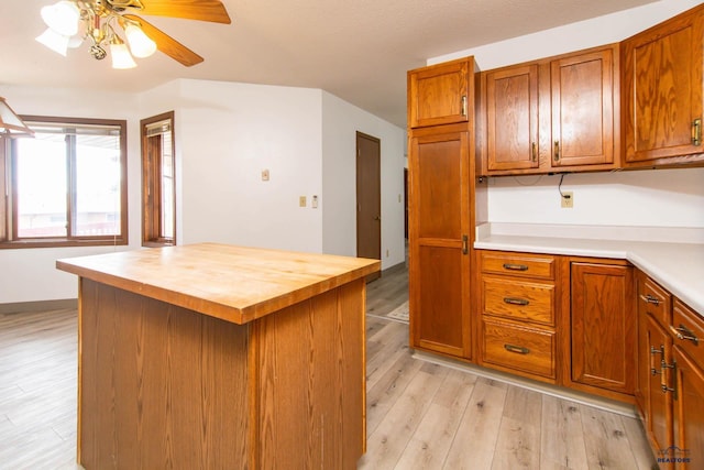 kitchen with a kitchen island, light wood-type flooring, ceiling fan, brown cabinets, and butcher block counters