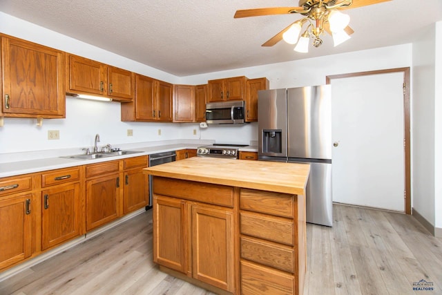 kitchen featuring wooden counters, a sink, stainless steel appliances, light wood-style floors, and a textured ceiling