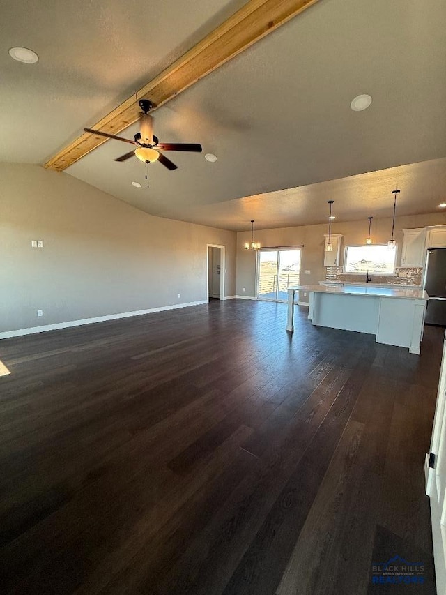 unfurnished living room with baseboards, dark wood finished floors, vaulted ceiling with beams, and ceiling fan with notable chandelier