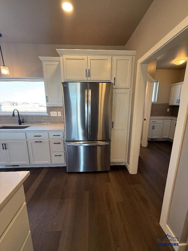 kitchen with dark wood-type flooring, a sink, backsplash, white cabinetry, and freestanding refrigerator