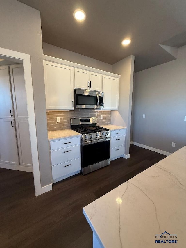 kitchen with light stone counters, dark wood-style floors, appliances with stainless steel finishes, white cabinets, and decorative backsplash