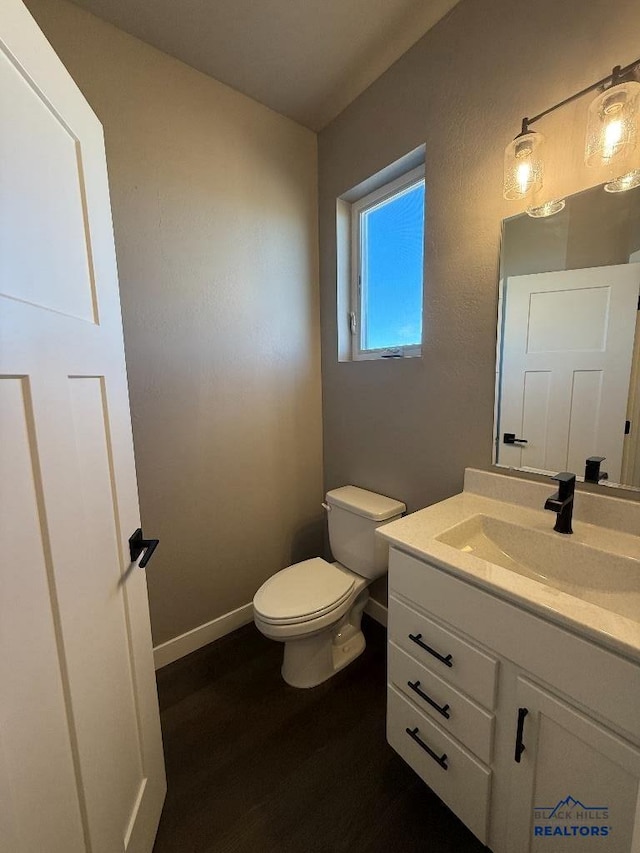 bathroom with toilet, vanity, baseboards, and wood finished floors