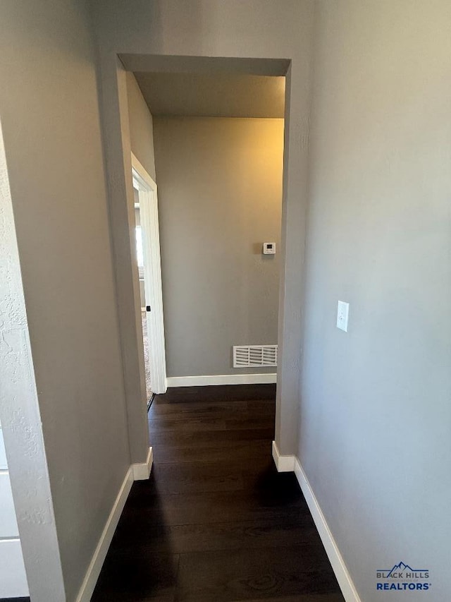 hall with visible vents, baseboards, and dark wood-style flooring