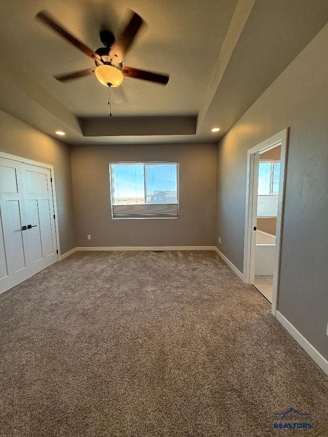 unfurnished bedroom with a tray ceiling, baseboards, and carpet