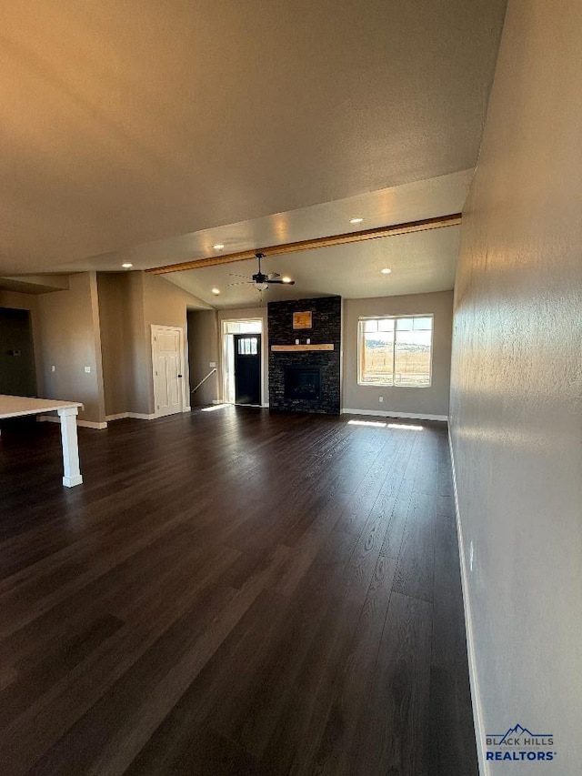 unfurnished living room featuring lofted ceiling with beams, baseboards, a stone fireplace, and dark wood-style floors