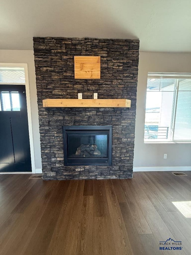 interior details with a stone fireplace, wood finished floors, visible vents, and baseboards