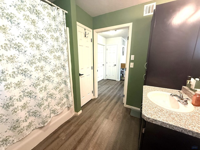 full bathroom with visible vents, baseboards, shower / tub combo, wood finished floors, and vanity