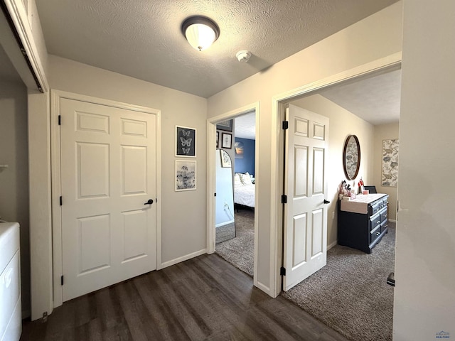 corridor with dark wood-type flooring, baseboards, and a textured ceiling