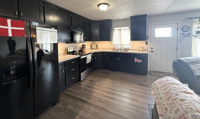 kitchen featuring dark wood finished floors, dark cabinets, light countertops, black appliances, and a sink