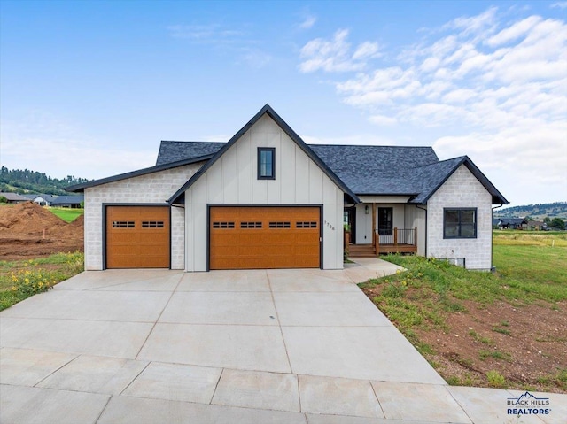 modern farmhouse with roof with shingles, a porch, concrete driveway, a garage, and board and batten siding