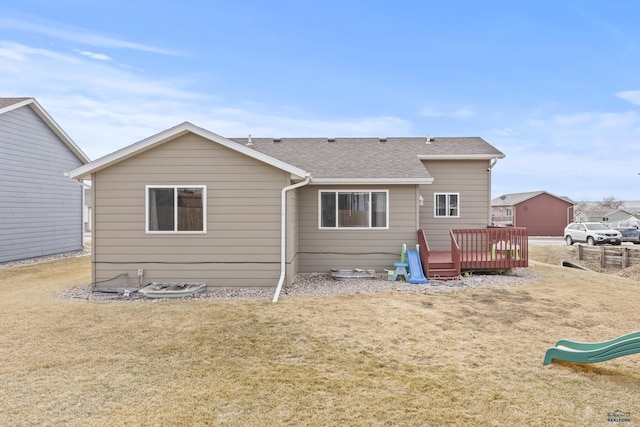 rear view of property featuring a deck, a yard, and roof with shingles