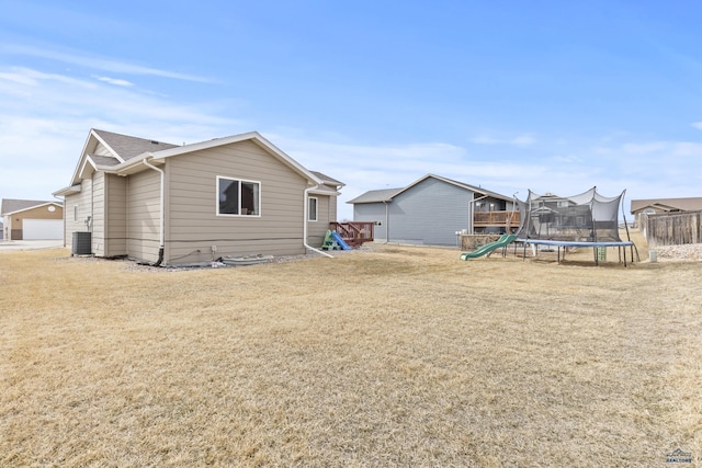 back of house with a yard, central AC unit, and a trampoline