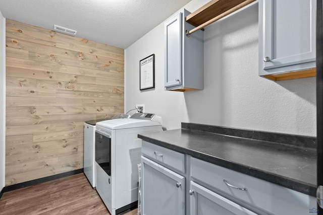 clothes washing area featuring visible vents, washing machine and clothes dryer, cabinet space, wood walls, and a textured ceiling
