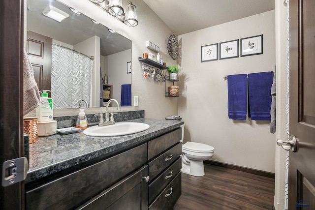 bathroom featuring baseboards, toilet, wood finished floors, and vanity
