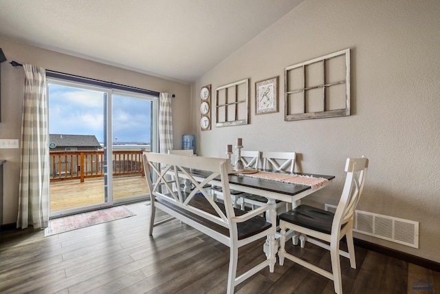 dining area featuring vaulted ceiling, wood finished floors, visible vents, and a textured wall
