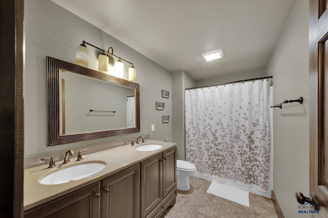 full bathroom with double vanity, tile patterned floors, toilet, and a sink