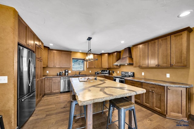 kitchen with a sink, a breakfast bar area, stainless steel appliances, wall chimney exhaust hood, and dark wood-style flooring