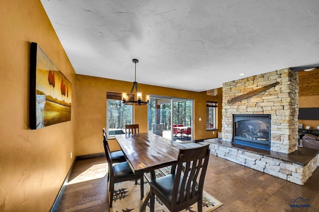 dining room with a notable chandelier, a fireplace, baseboards, and hardwood / wood-style floors