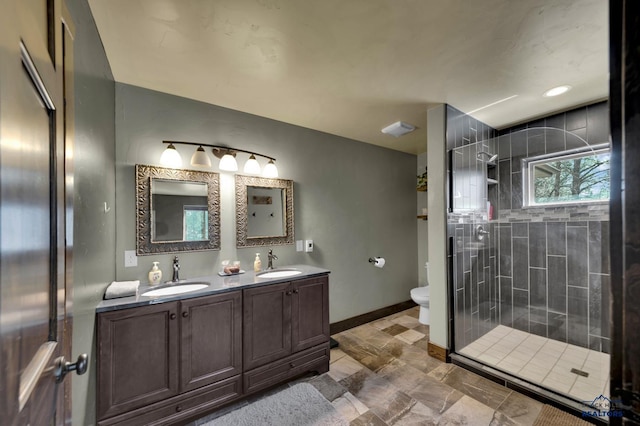 bathroom featuring double vanity, a shower stall, toilet, and a sink