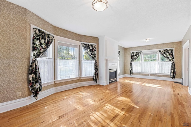 1120 W Blvd, Rapid City, SD 57701 - unfurnished living room featuring a glass covered fireplace, wallpapered walls, light wood-type flooring, and baseboards