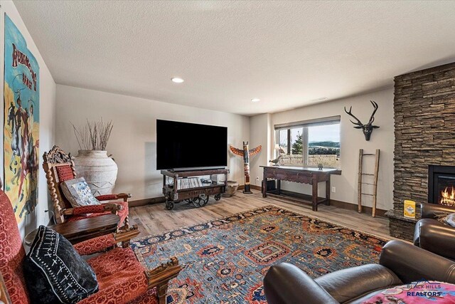 living room with a stone fireplace, a textured ceiling, baseboards, and wood finished floors