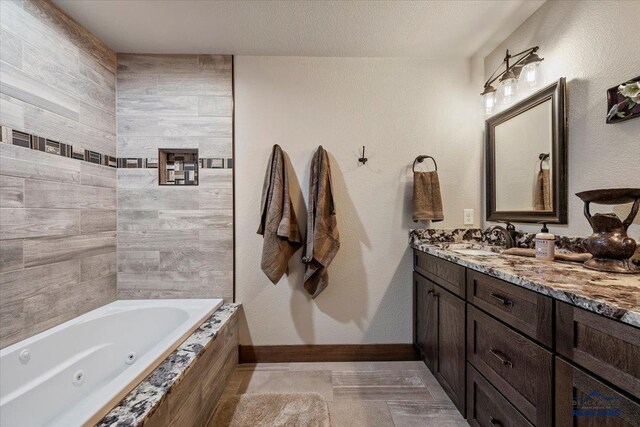 full bath with a textured ceiling, a jetted tub, vanity, and baseboards